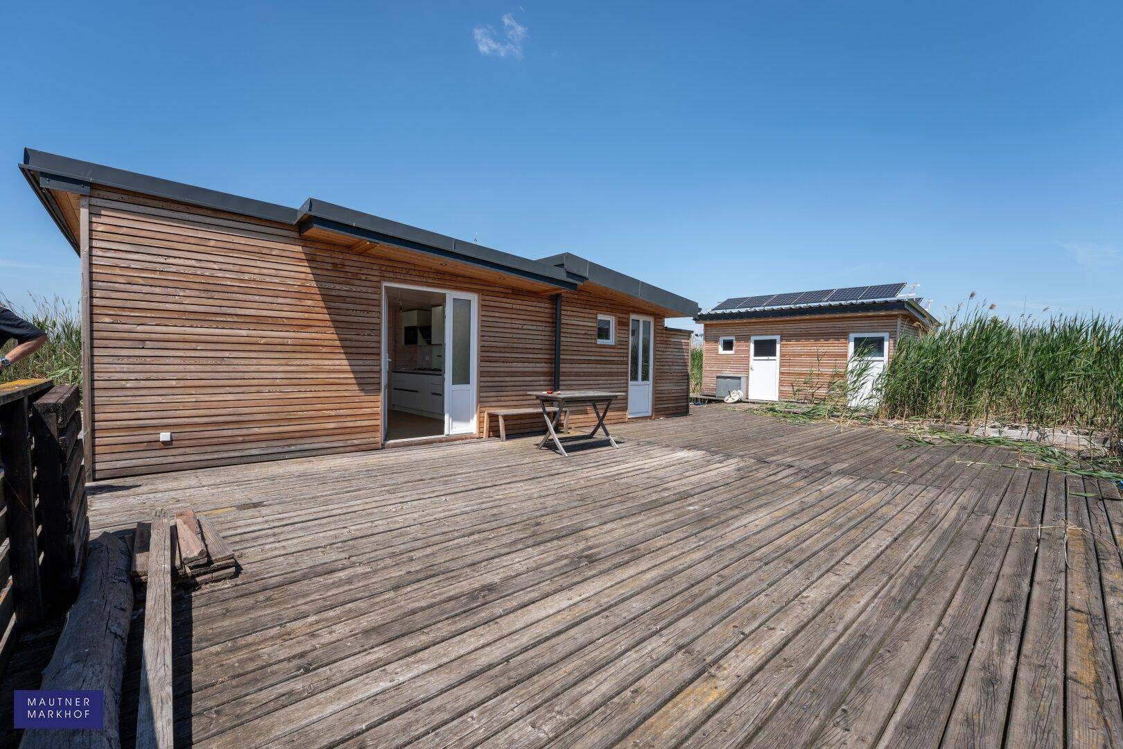Weitläufige Holzterrasse vor dem modernen Holzhaus mit Blick auf das Wasser.