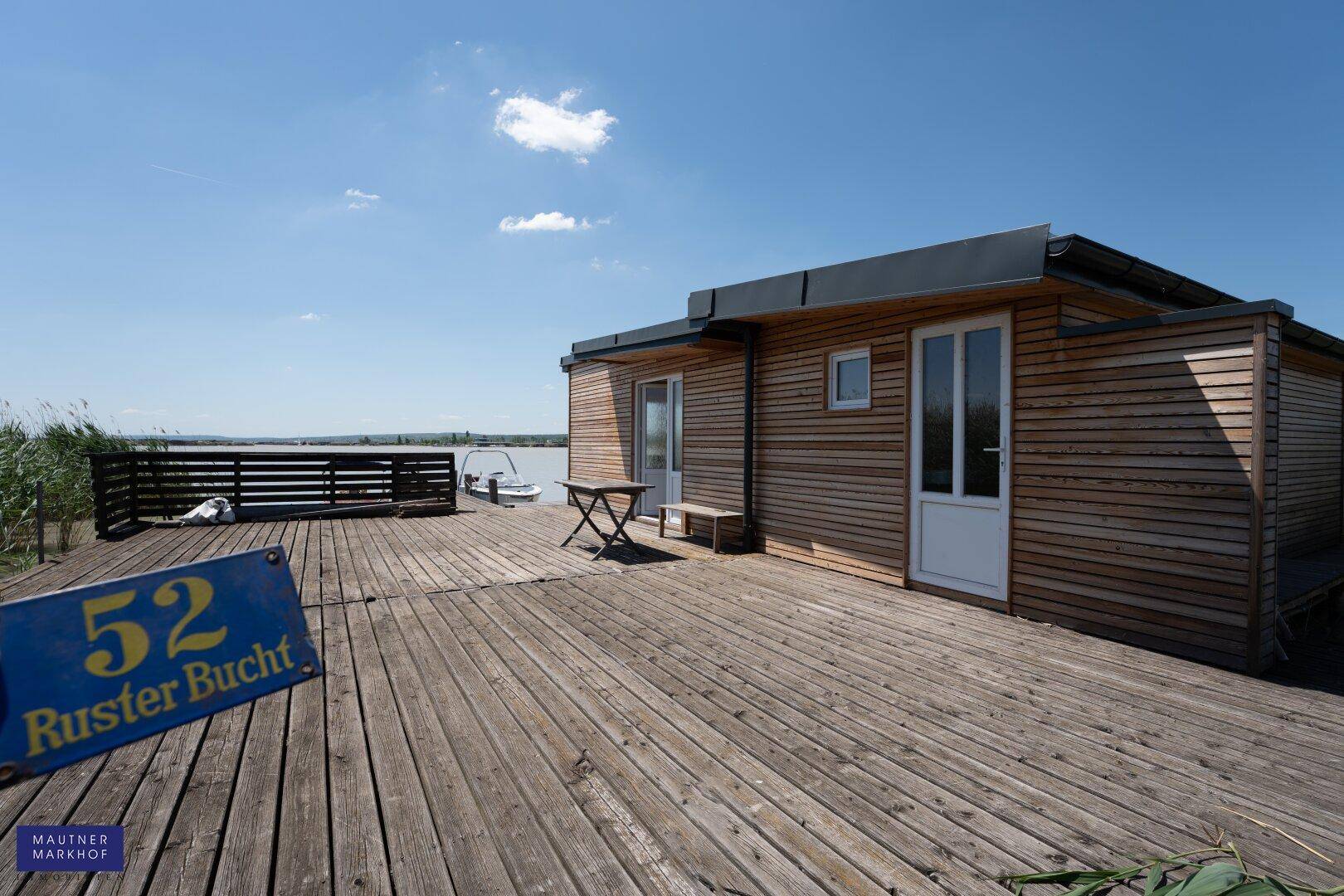 Große Holzterrasse am Wasser mit Blick auf den See und einem kleinen Tisch.