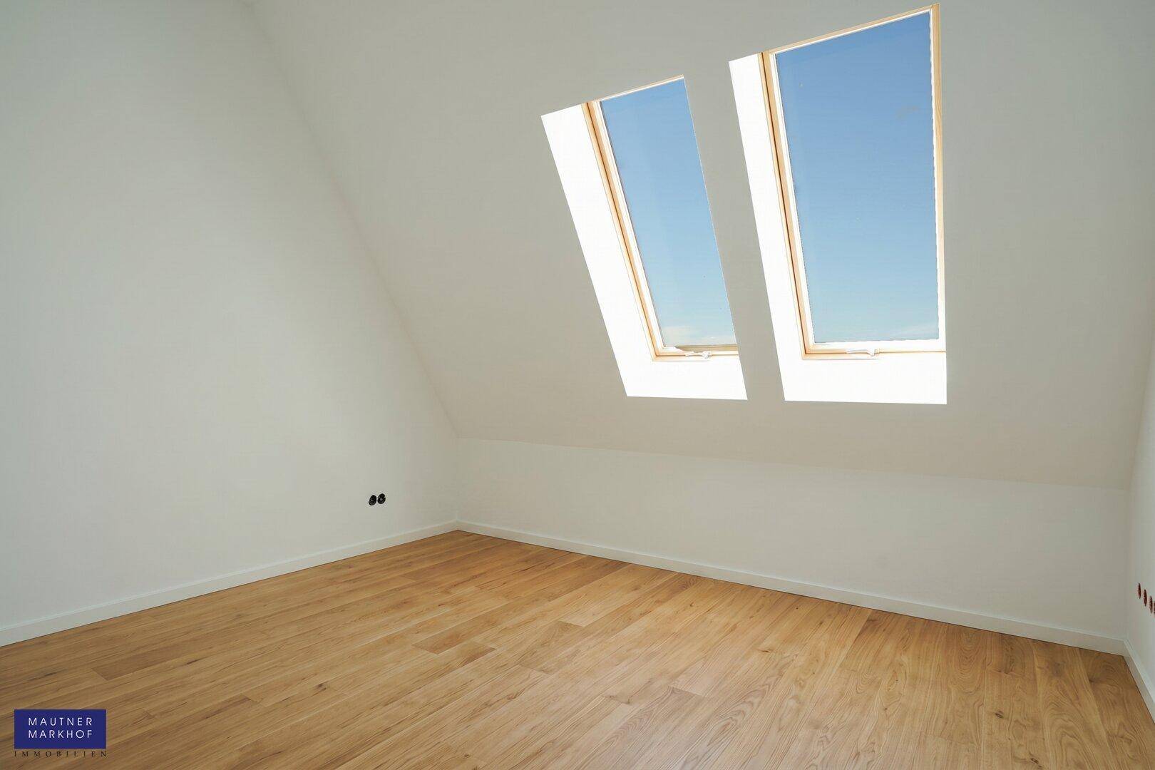 Dachzimmer mit hellem Holzboden und zwei großen Dachfenstern, die den Raum lichtdurchfluten.