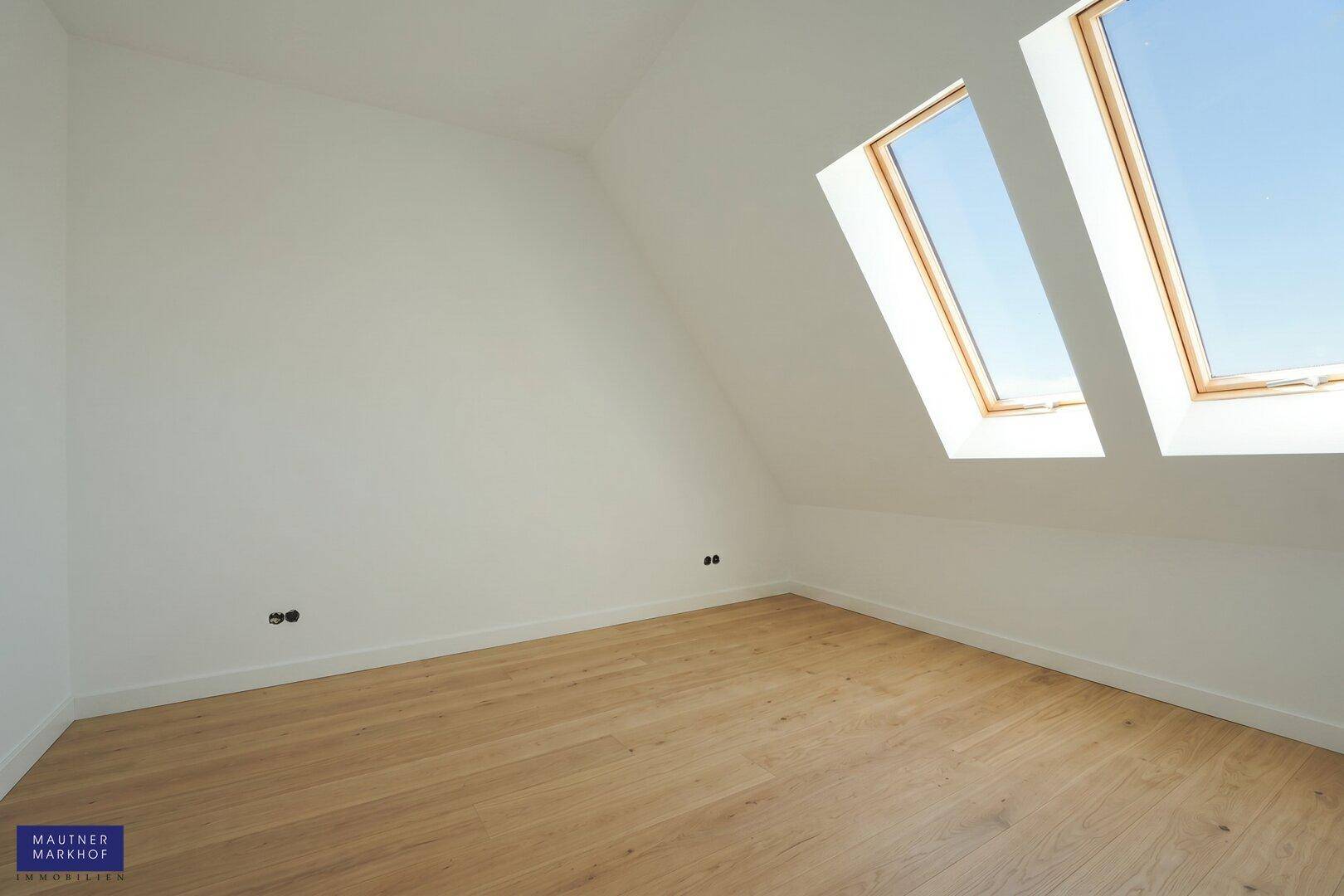 Helles Dachzimmer mit Holzboden und zwei großen Dachfenstern, die für viel natürliches Licht sorgen.