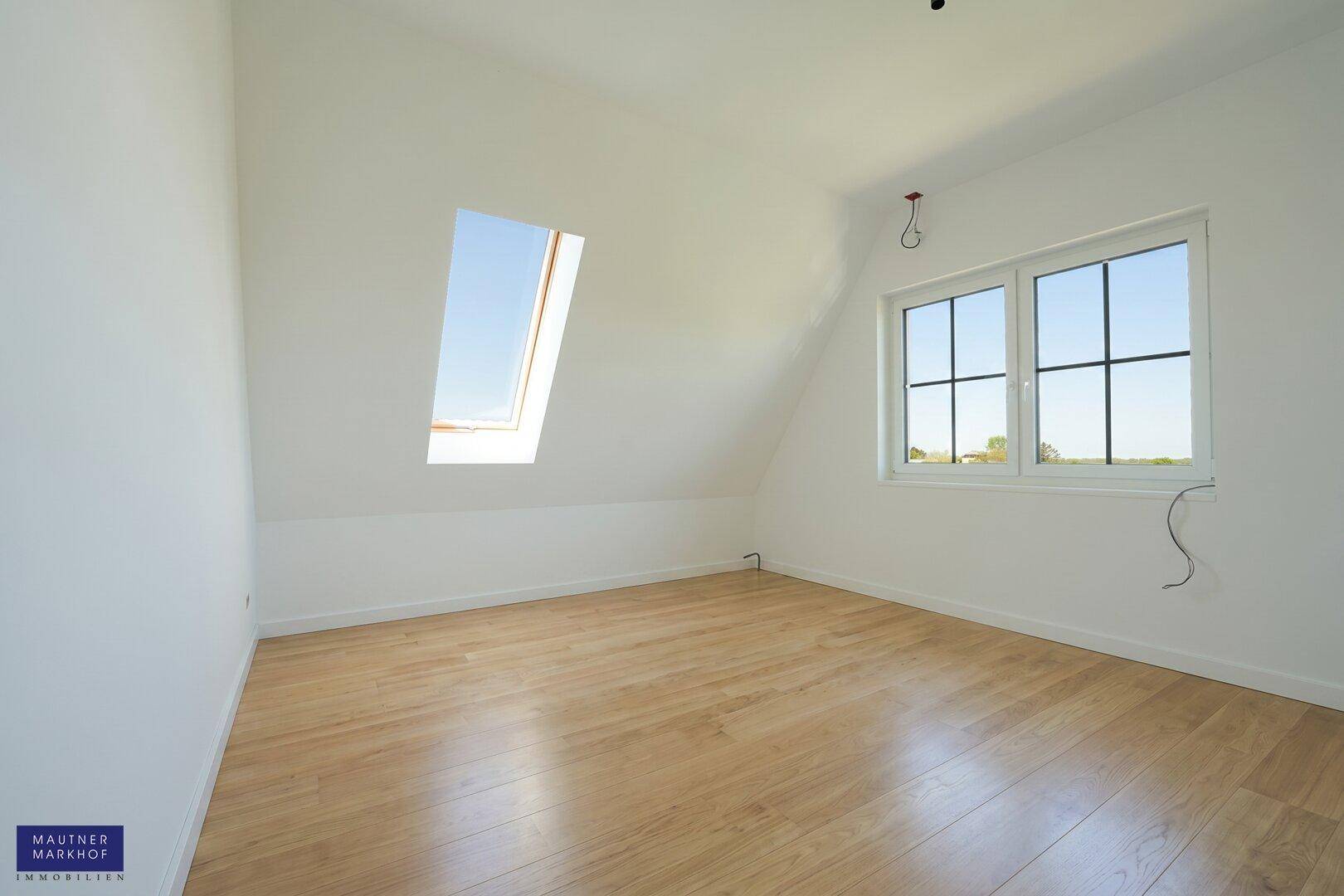 Dachzimmer mit Holzboden, einem Dachfenster und einem normalen Fenster mit Blick ins Grüne.