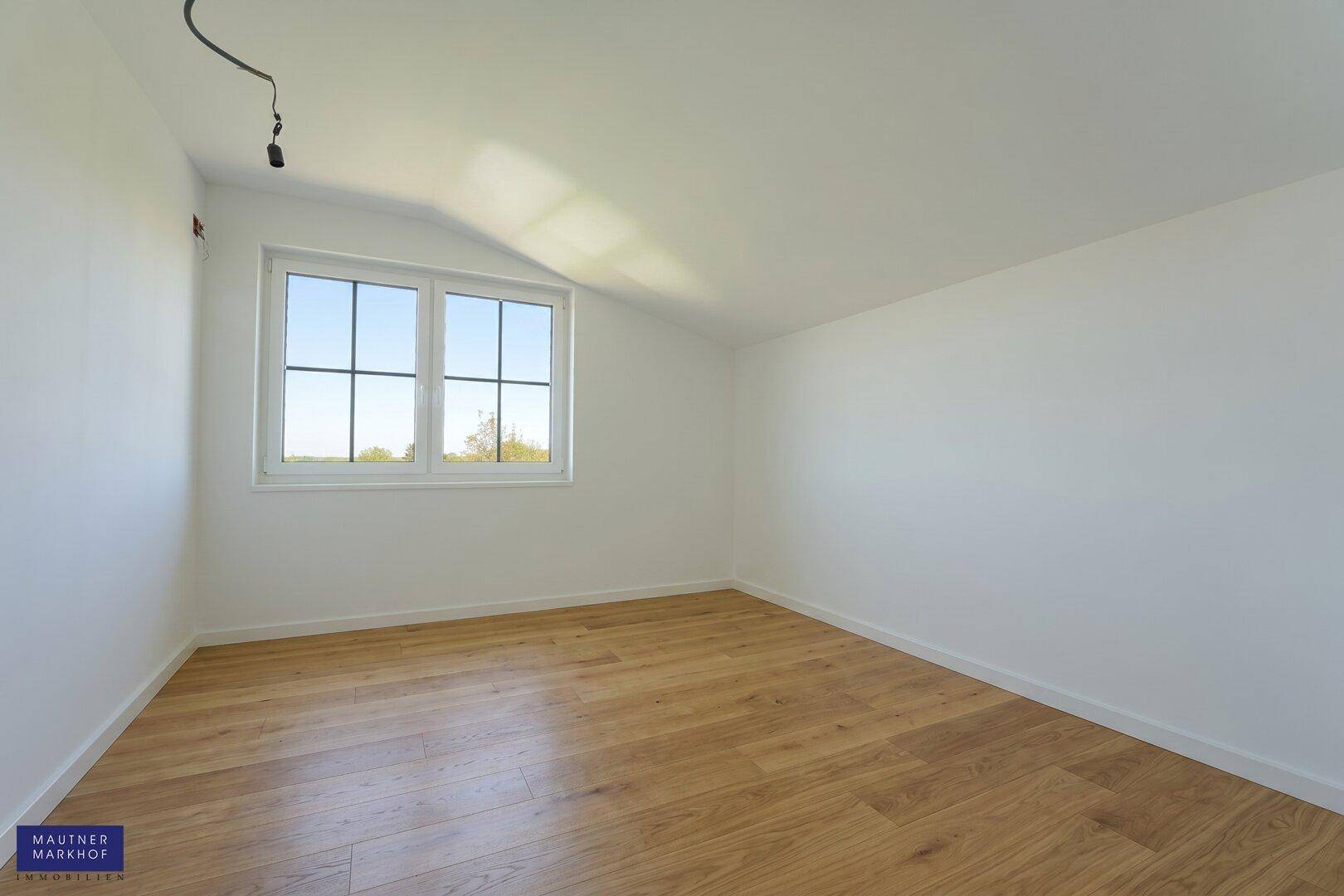 Helles Schlafzimmer mit Holzboden und einem großen Fenster, das einen schönen Blick ins Grüne bietet.