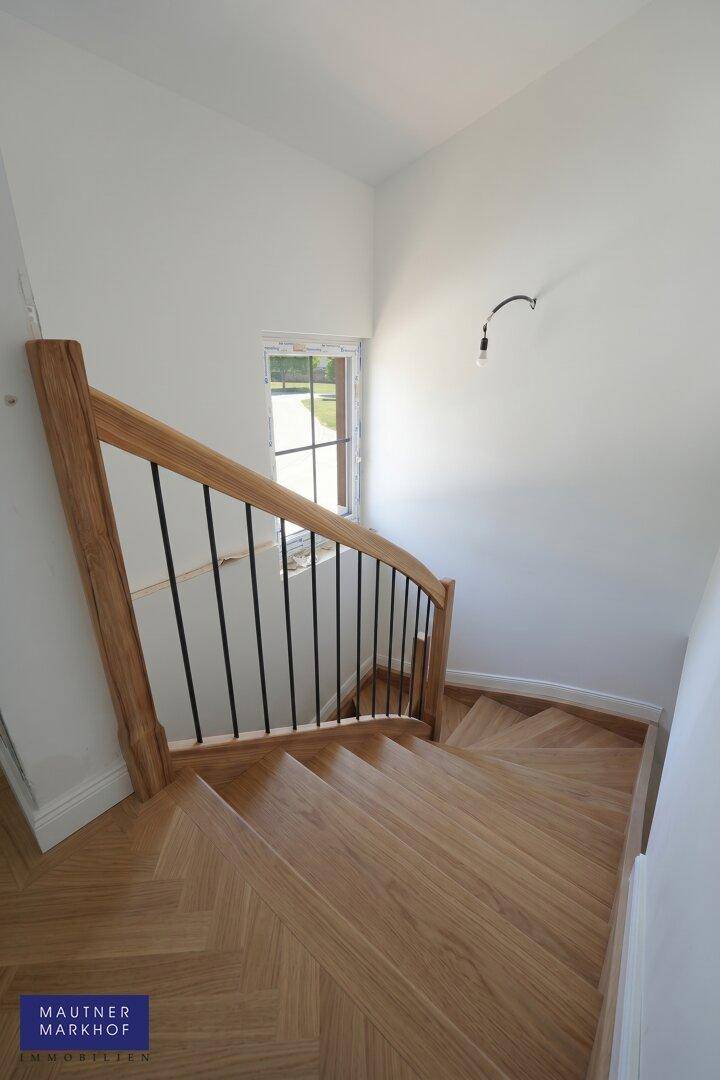 Elegante Holztreppe mit schwarzem Geländer, die zu den oberen Etagen führt und gut beleuchtet ist.