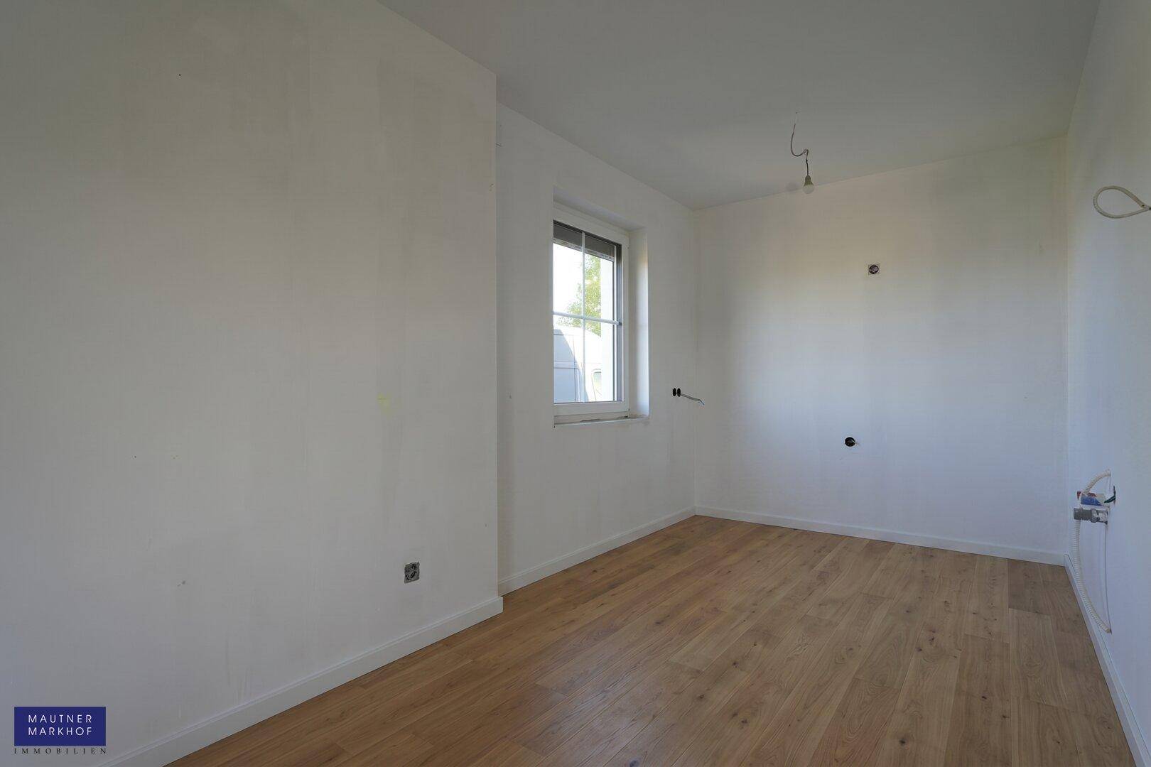 Leeres Zimmer mit hellem Holzboden und einem Fenster, das den Raum mit Tageslicht versorgt.