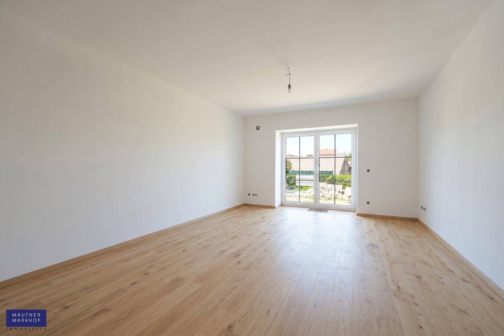 Helles Zimmer mit Holzboden und einer großen Terrassentür, die viel Tageslicht hereinlässt.