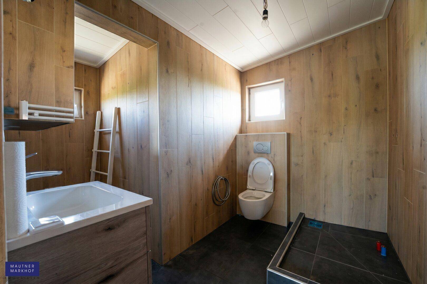 Modernes Badezimmer mit Holzwandverkleidung, wandhängendem WC und Dusche.