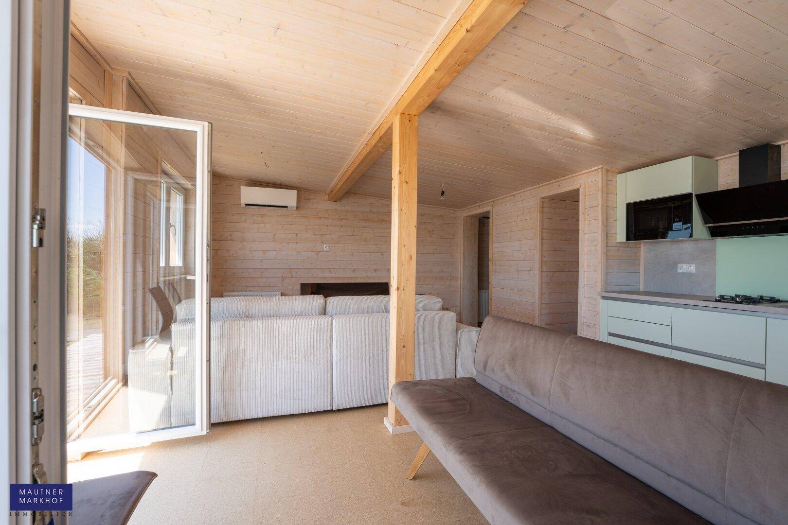 Offener Wohnbereich mit Holzwänden, moderner Küche und Zugang zur Terrasse.