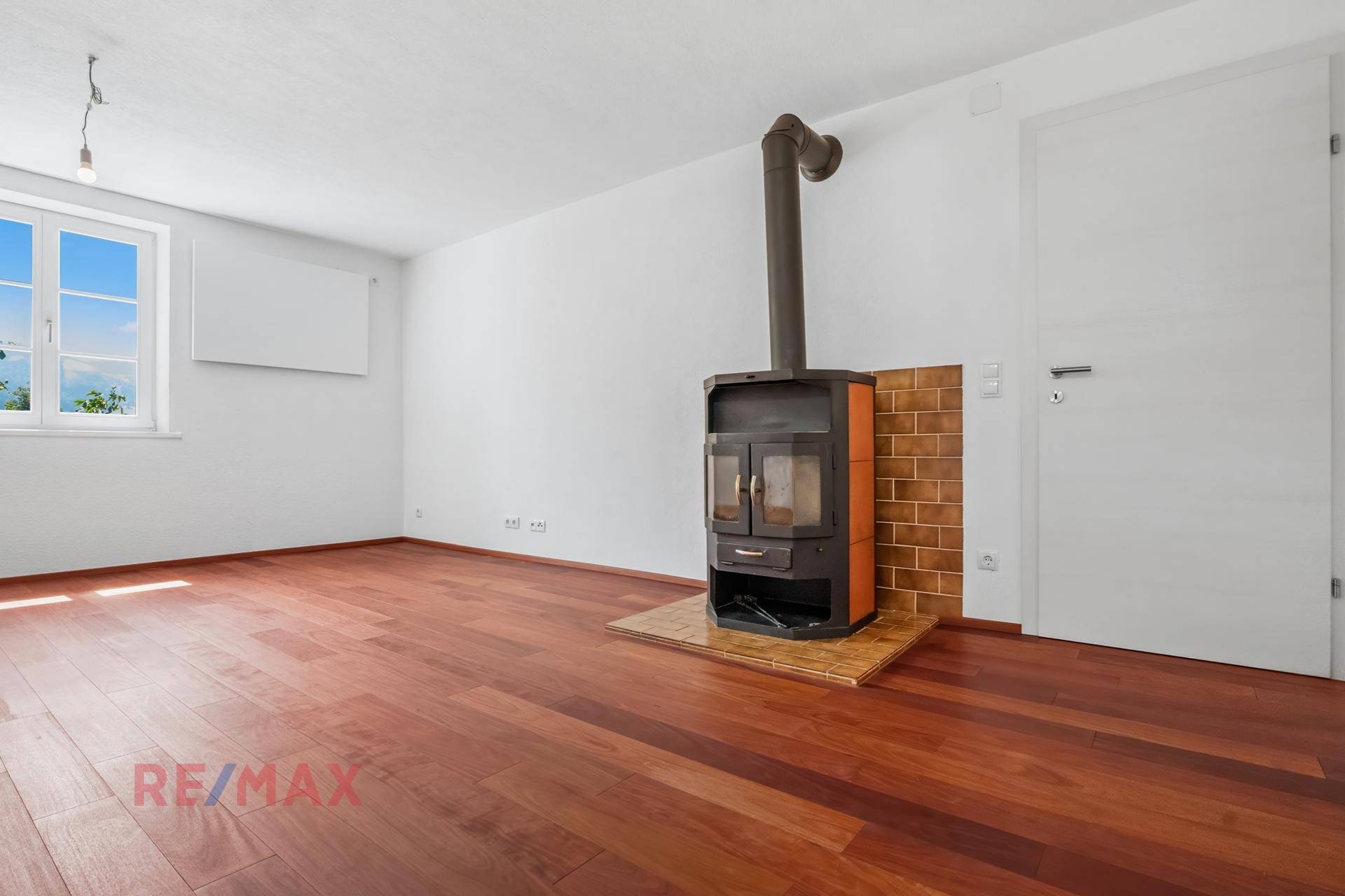 Detailaufnahme des Holzofens im Wohnzimmer, umgeben von Holzboden und einem Fenster.