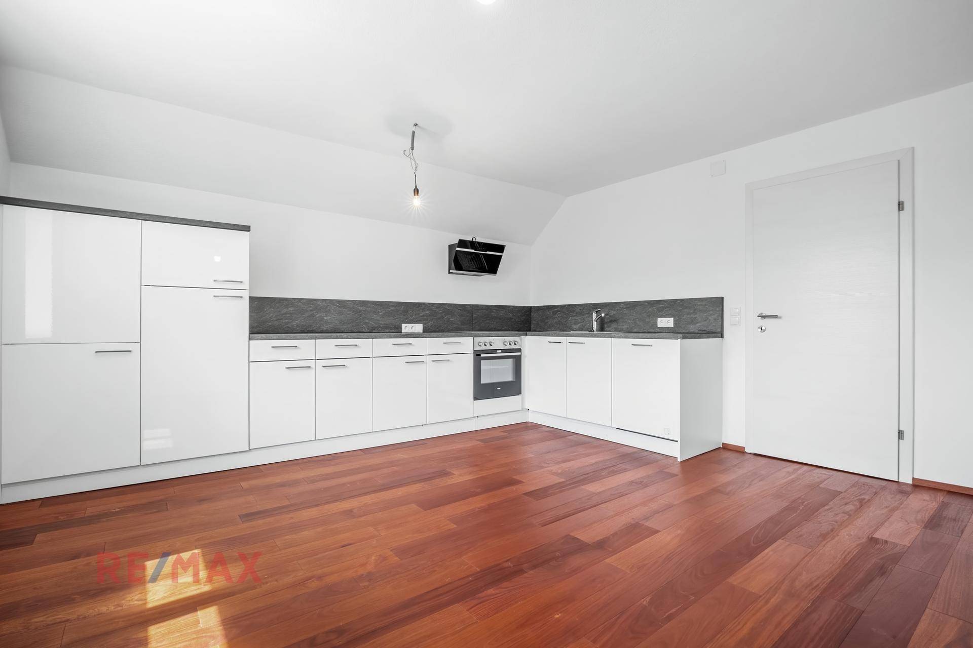 Moderne Einbauküche mit weißen Hochglanzfronten und dunkler Arbeitsplatte, kombiniert mit warmem Holzboden.