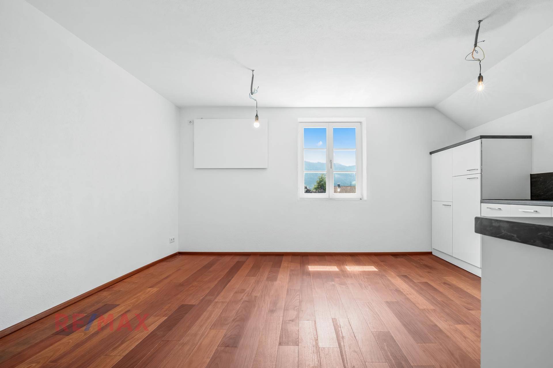 Heller Raum mit Holzboden und einem Fenster, das einen weiten Blick auf die Berge bietet.
