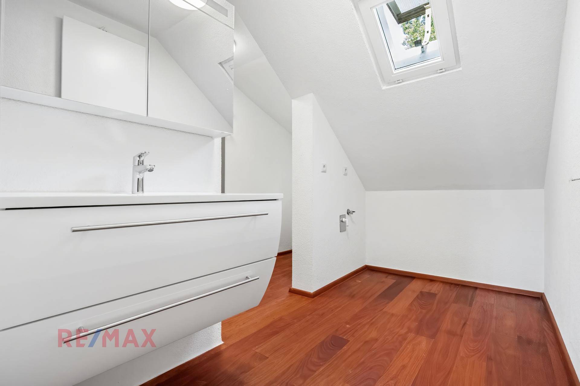 Modernes Badezimmer mit Waschtisch, Spiegelschrank und Dachfenster für natürliches Licht.