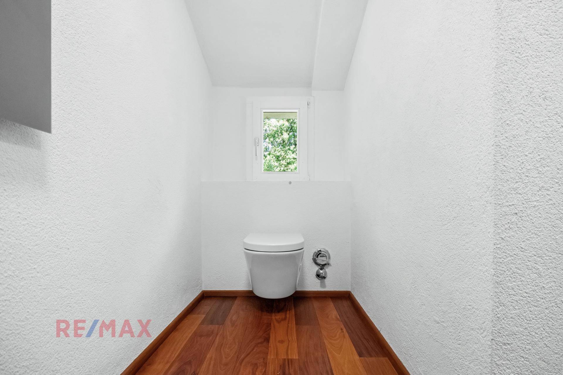 Separates WC mit wandhängender Toilette und einem Fenster für Belüftung und Tageslicht.