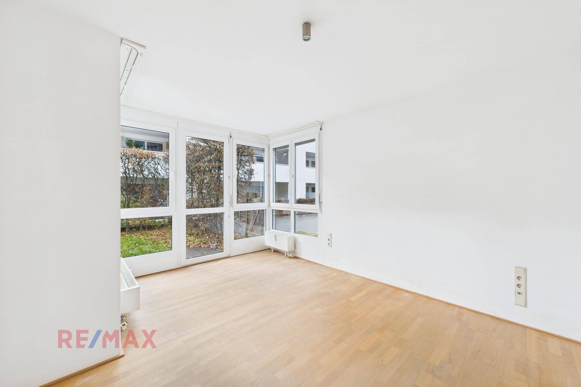 Heller Raum mit großen Fenstern, die einen Blick in den Garten ermöglichen, und Holzboden.