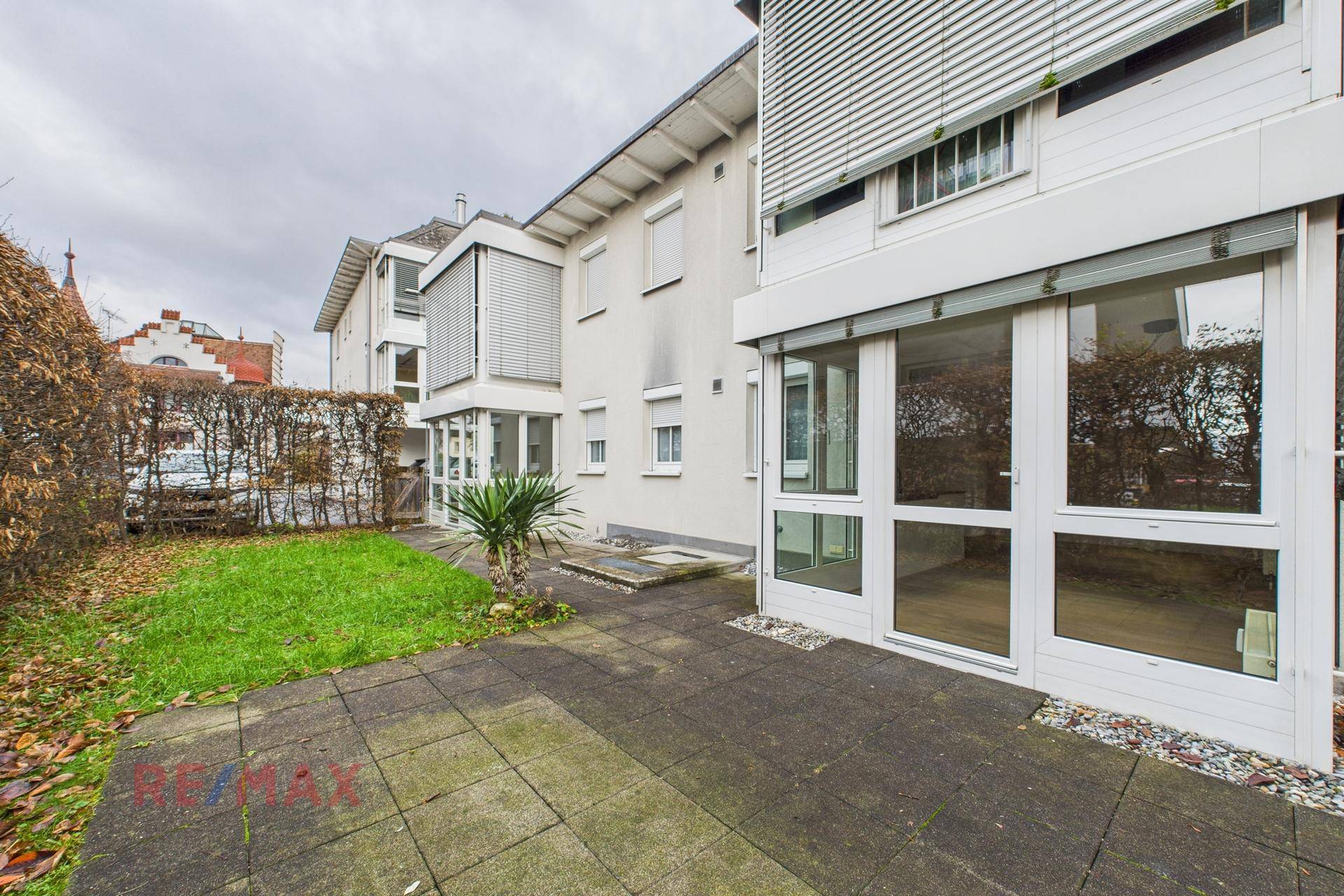 Außenbereich mit gepflasterter Terrasse, kleinem Rasenstück und Hecke als Sichtschutz.