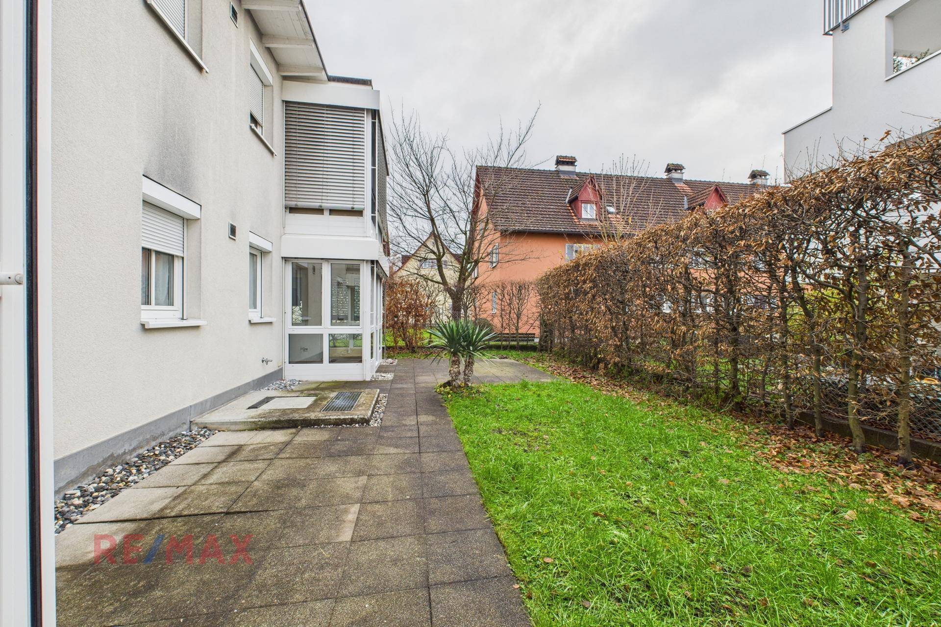 Seitlicher Gartenbereich mit Terrasse, Rasenfläche und hoher Hecke für Privatsphäre.