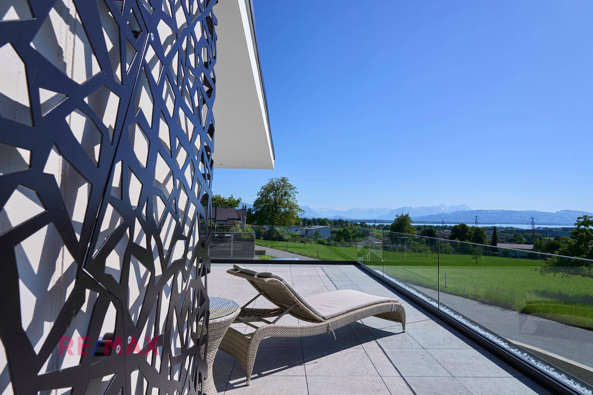 Sonniger Terrassenbereich mit Liegestuhl, dekorativem Sichtschutz und weitem Blick auf die Umgebung.