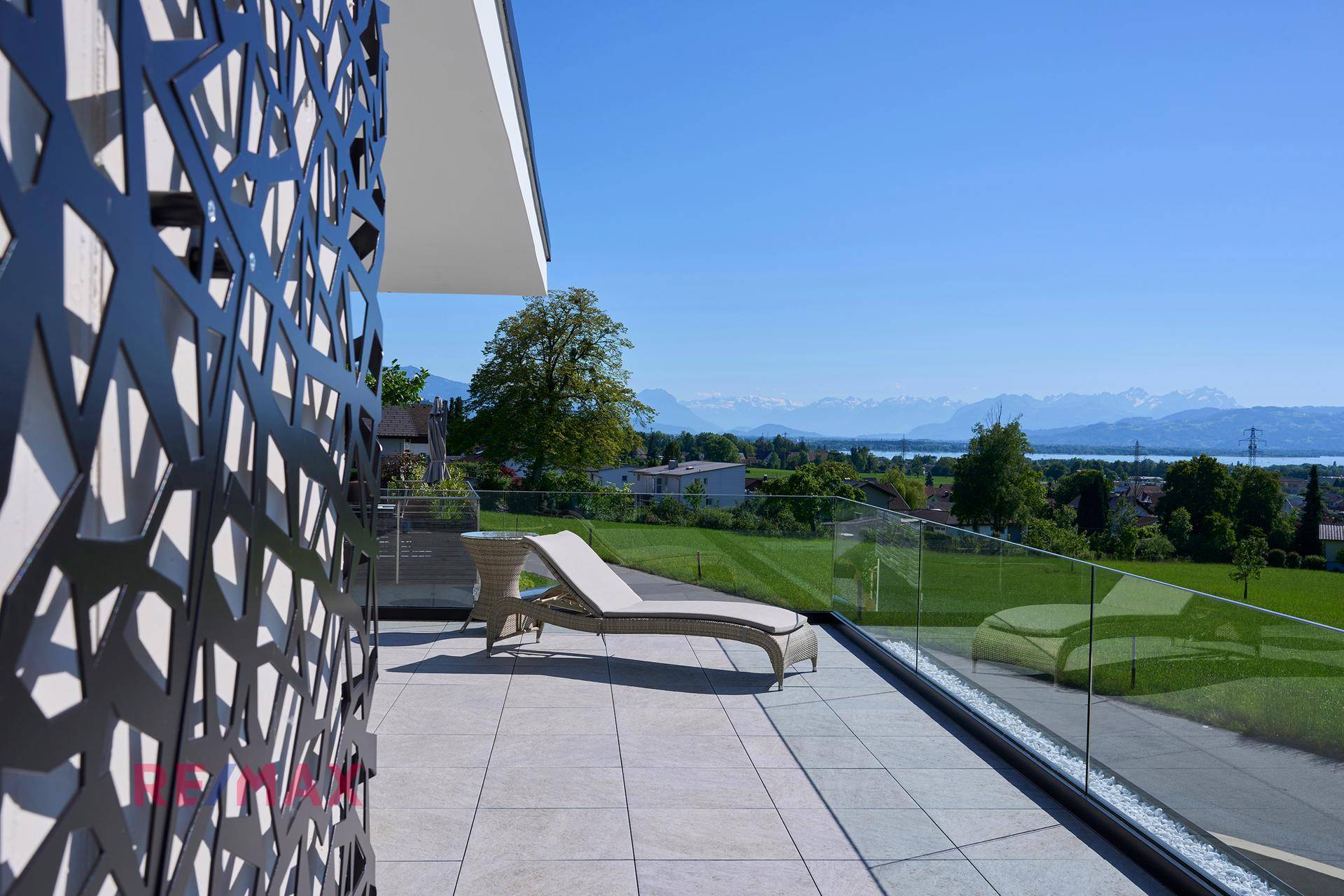 Geräumige Terrasse mit Liegestuhl, modernem Sichtschutz und Panoramablick auf See und Berge.