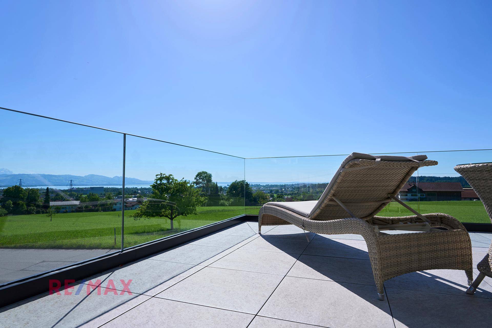 Offene Terrasse mit Glasgeländer und unverbautem Blick auf die grüne Landschaft und den See.