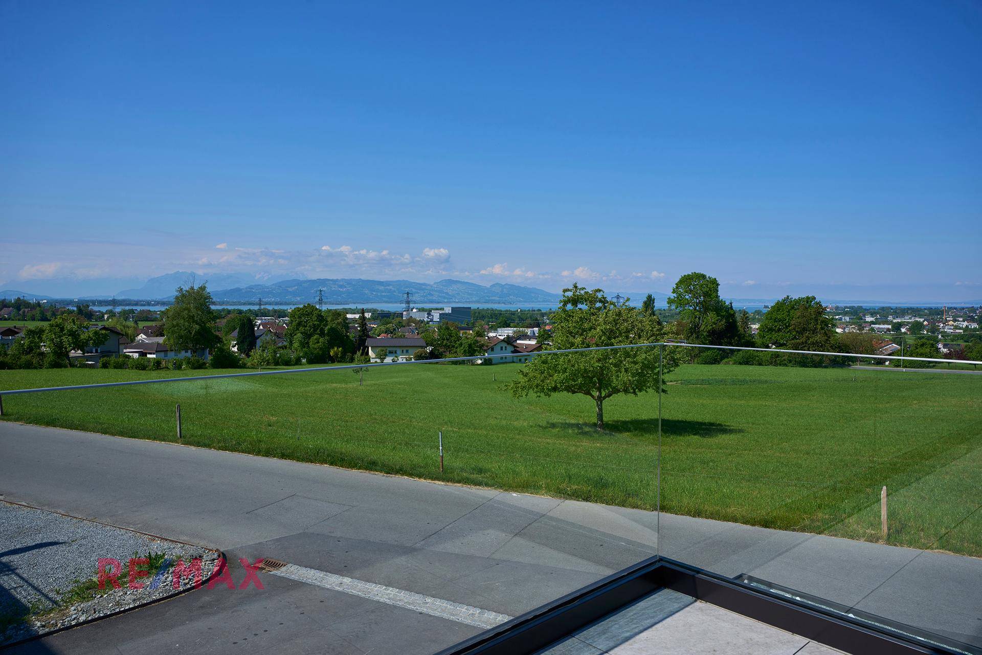 Weitläufiger Blick über grüne Felder, den See und die umliegende Bebauung an einem sonnigen Tag.
