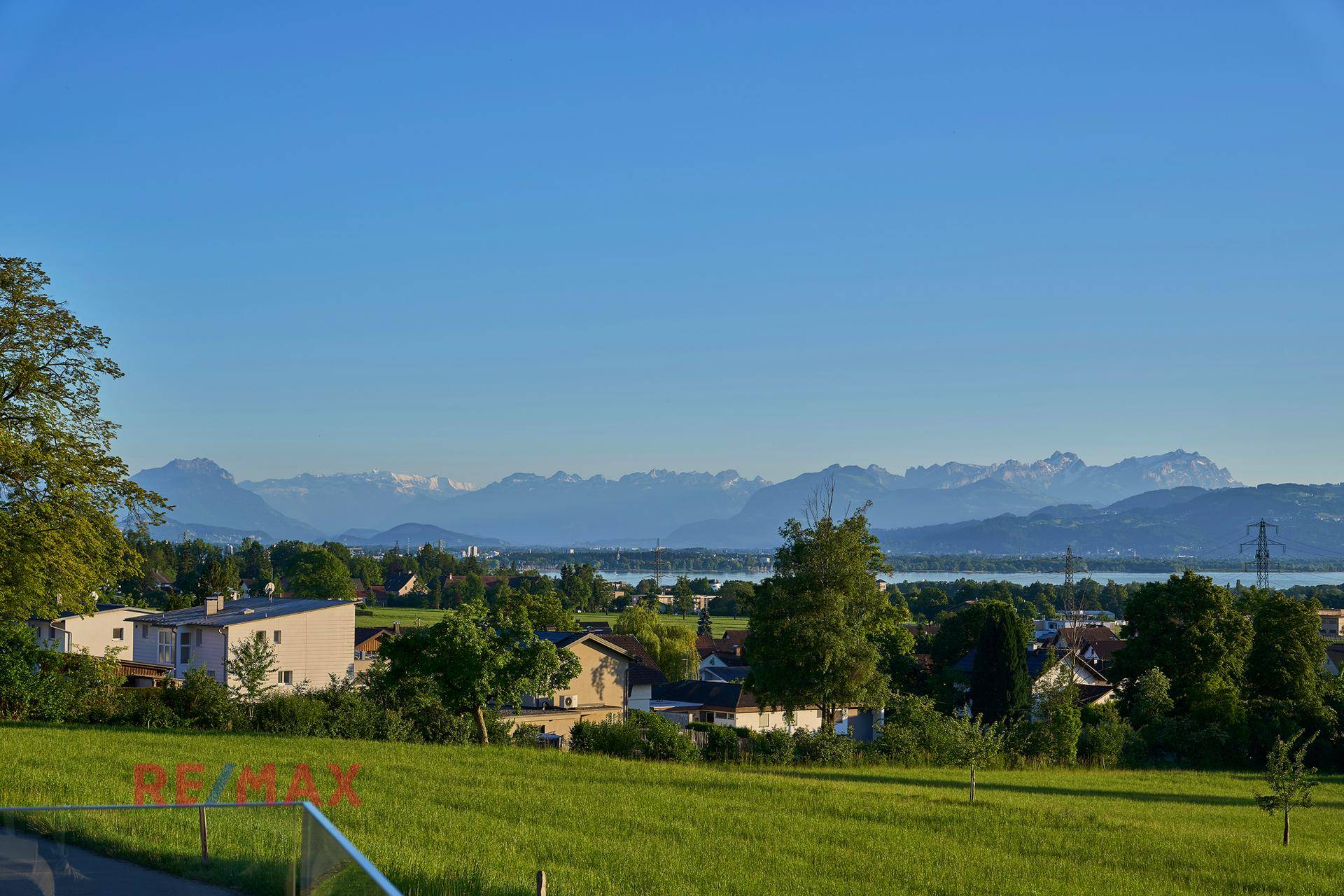 Malerischer Ausblick auf die grüne Landschaft, den See und die fernen Berge bei Sonnenuntergang.