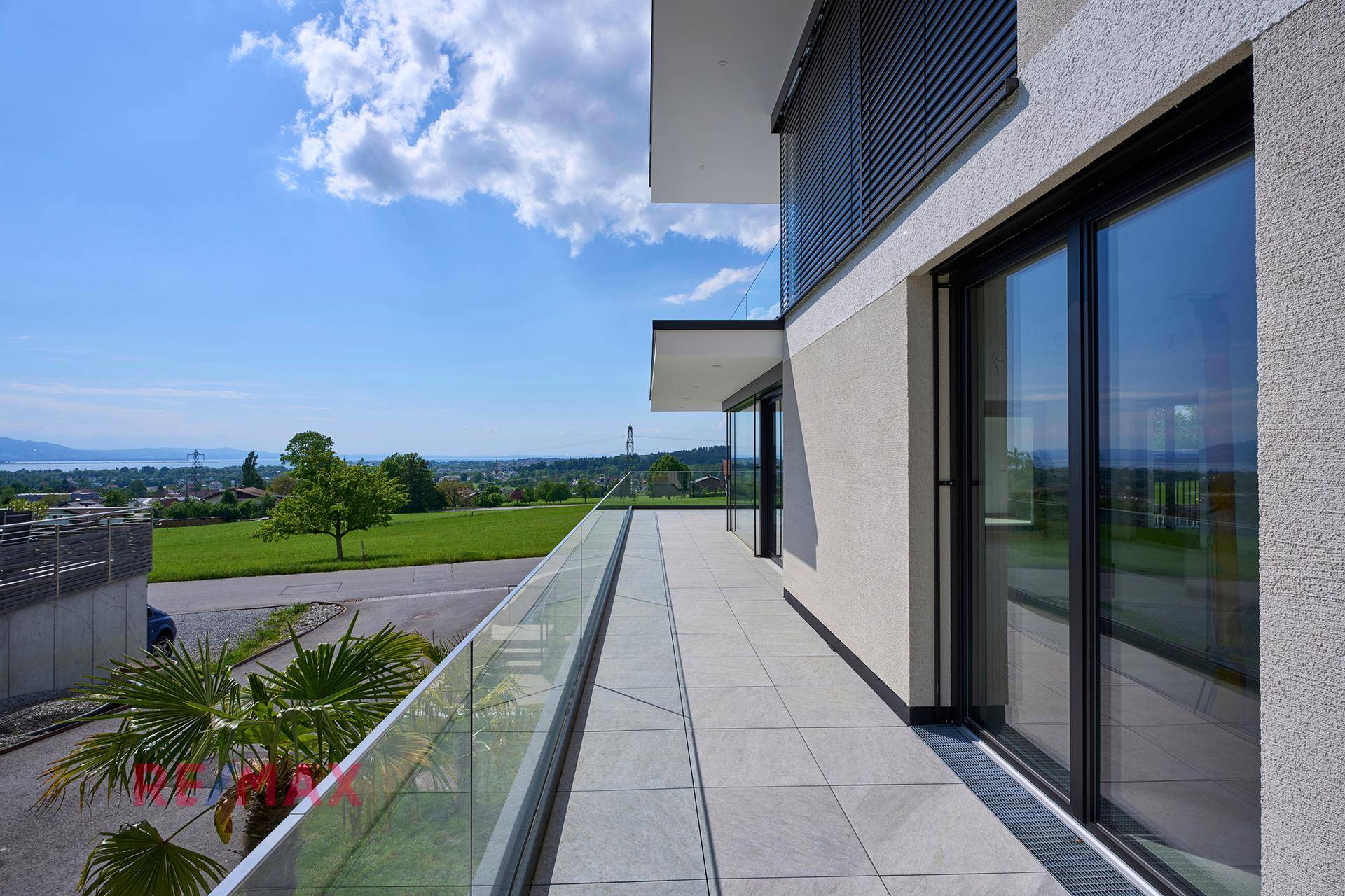 Langer Balkon mit Glasgeländer und weitem Blick über die Landschaft und den See.