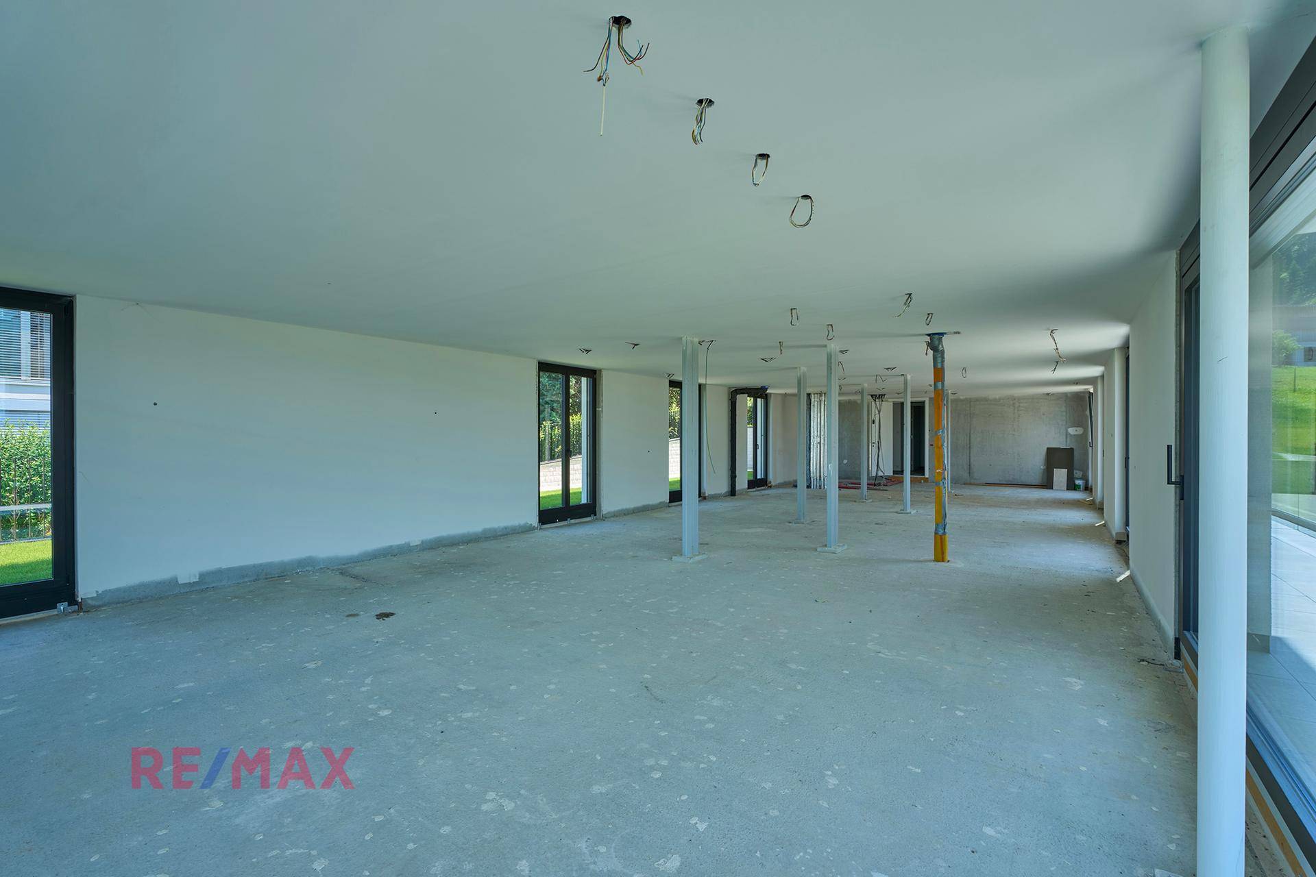 Weitläufiger, unfertiger Innenraum mit zahlreichen Fenstern und Blick auf die Natur.