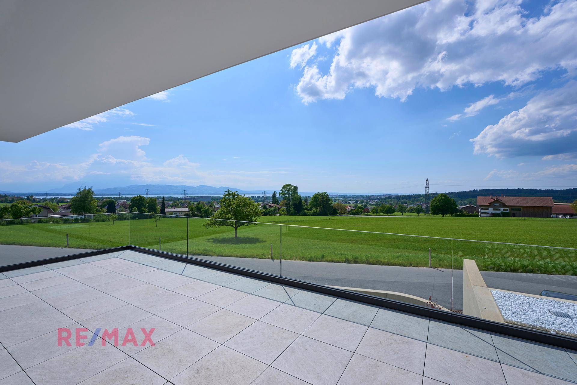 Sonniger Terrassenbereich mit Glasgeländer und weitem Blick über die grüne Landschaft.