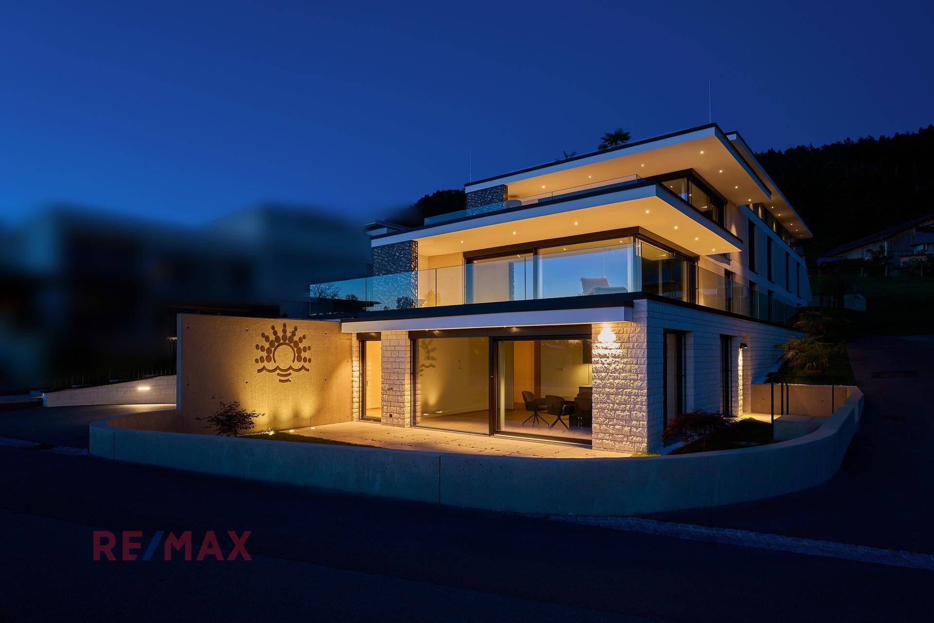 Modernes Wohngebäude bei Nacht, beleuchtet mit warmem Licht und Blick auf die Umgebung.