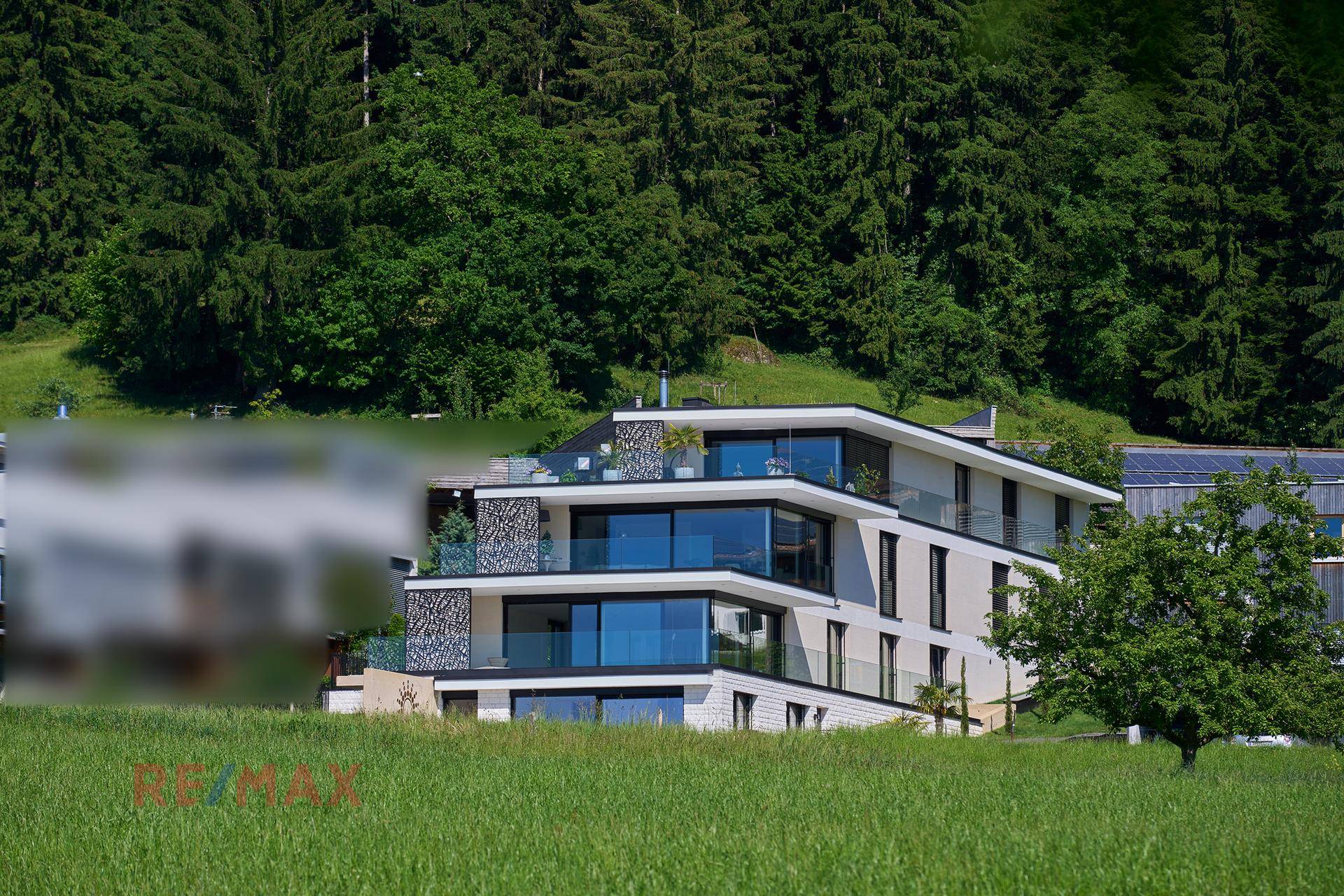 Modernes Mehrfamilienhaus mit Terrassen und großen Glasflächen, eingebettet in grüne Landschaft.