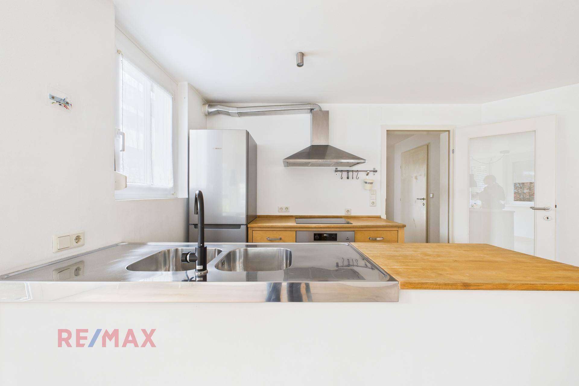 Detailansicht der modernen Küche mit Edelstahlspüle, Holzarbeitsplatte und Kühlschrank.