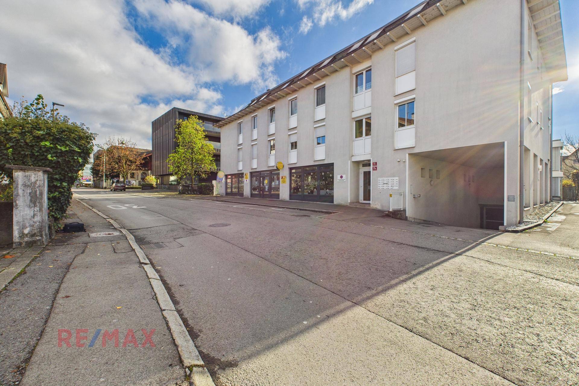 Mehrfamilienhaus mit Geschäften im Erdgeschoss und Parkmöglichkeiten an der Straße.