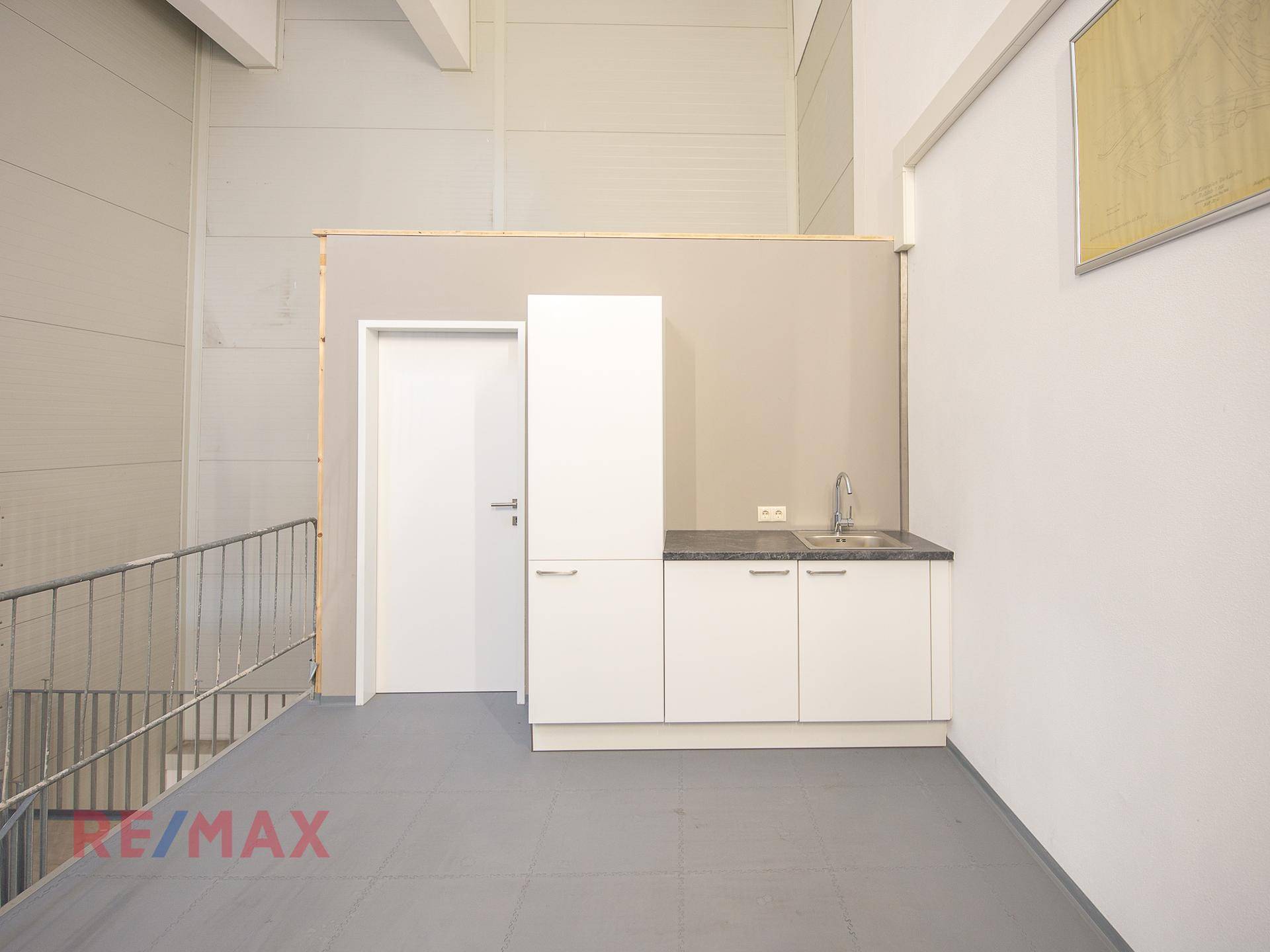 Kleine Küchenzeile mit Spüle und Schränken neben einer modernen Metalltreppe in einem hohen Raum.