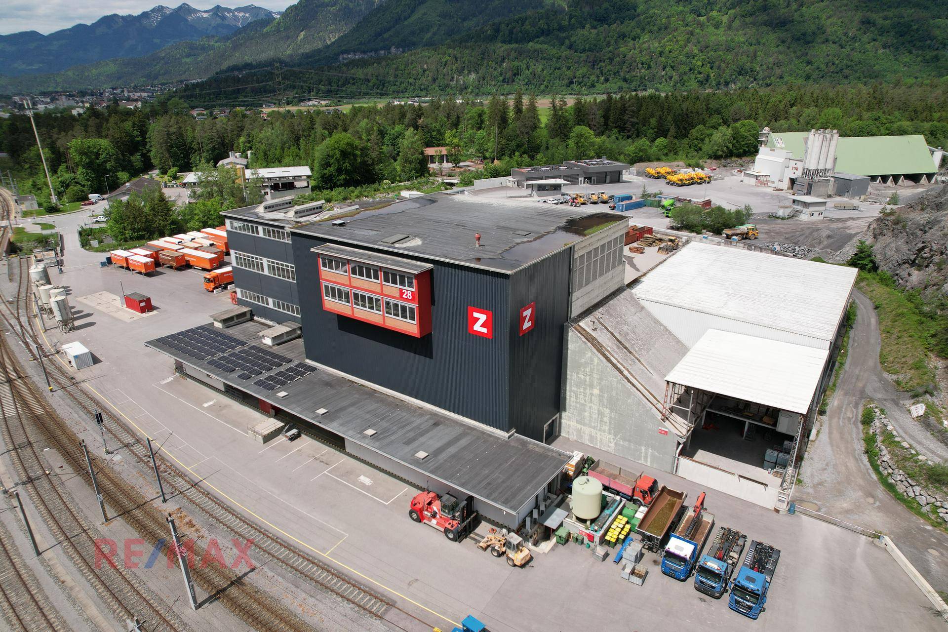 Industriekomplex mit Flachdach, Solaranlage und Laderampen, umgeben von Natur und Bahninfrastruktur.