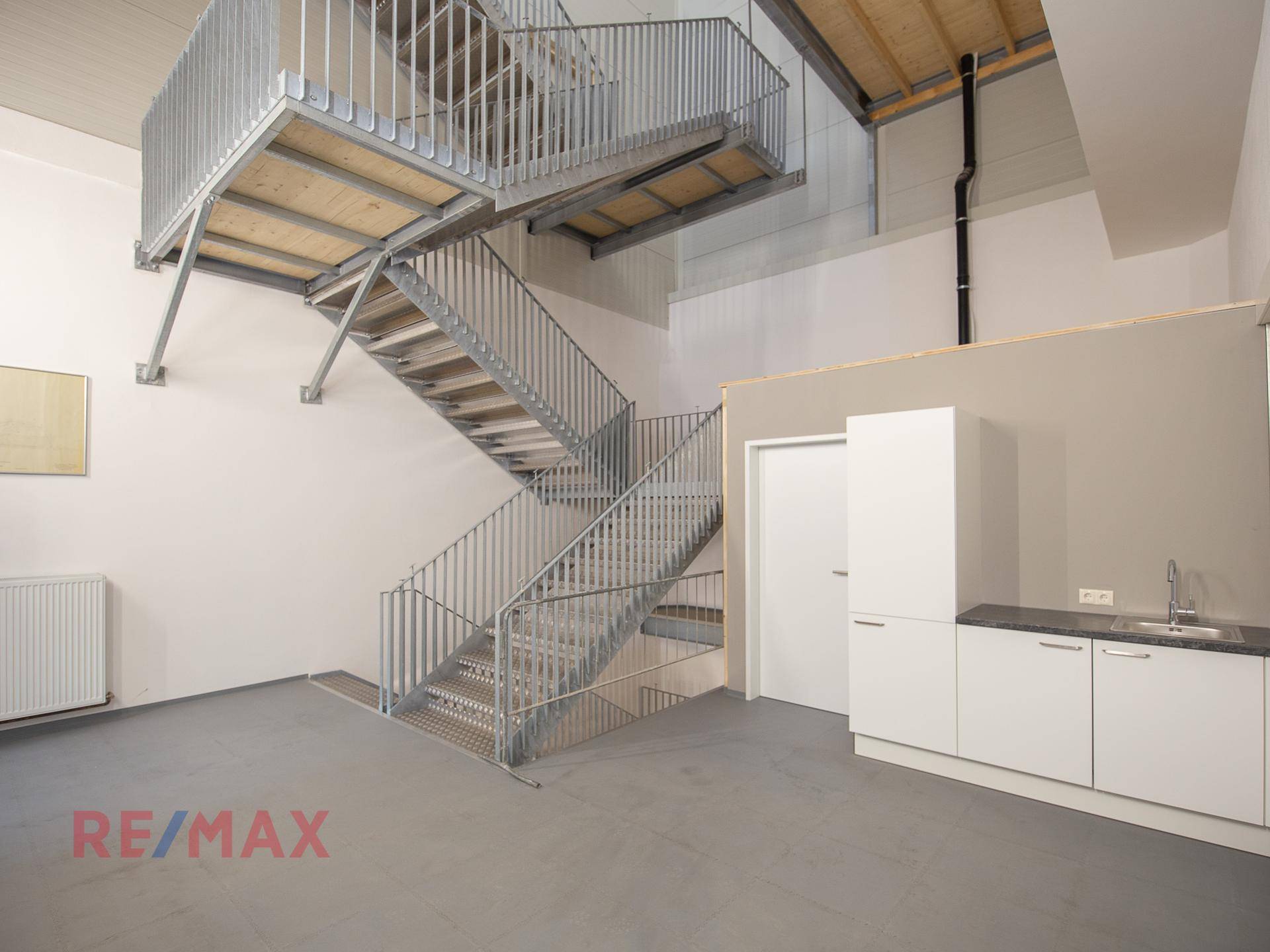 Mehrstöckige Metalltreppe in einem hohen Raum mit einer funktionalen Küchenzeile und hellen Wänden.
