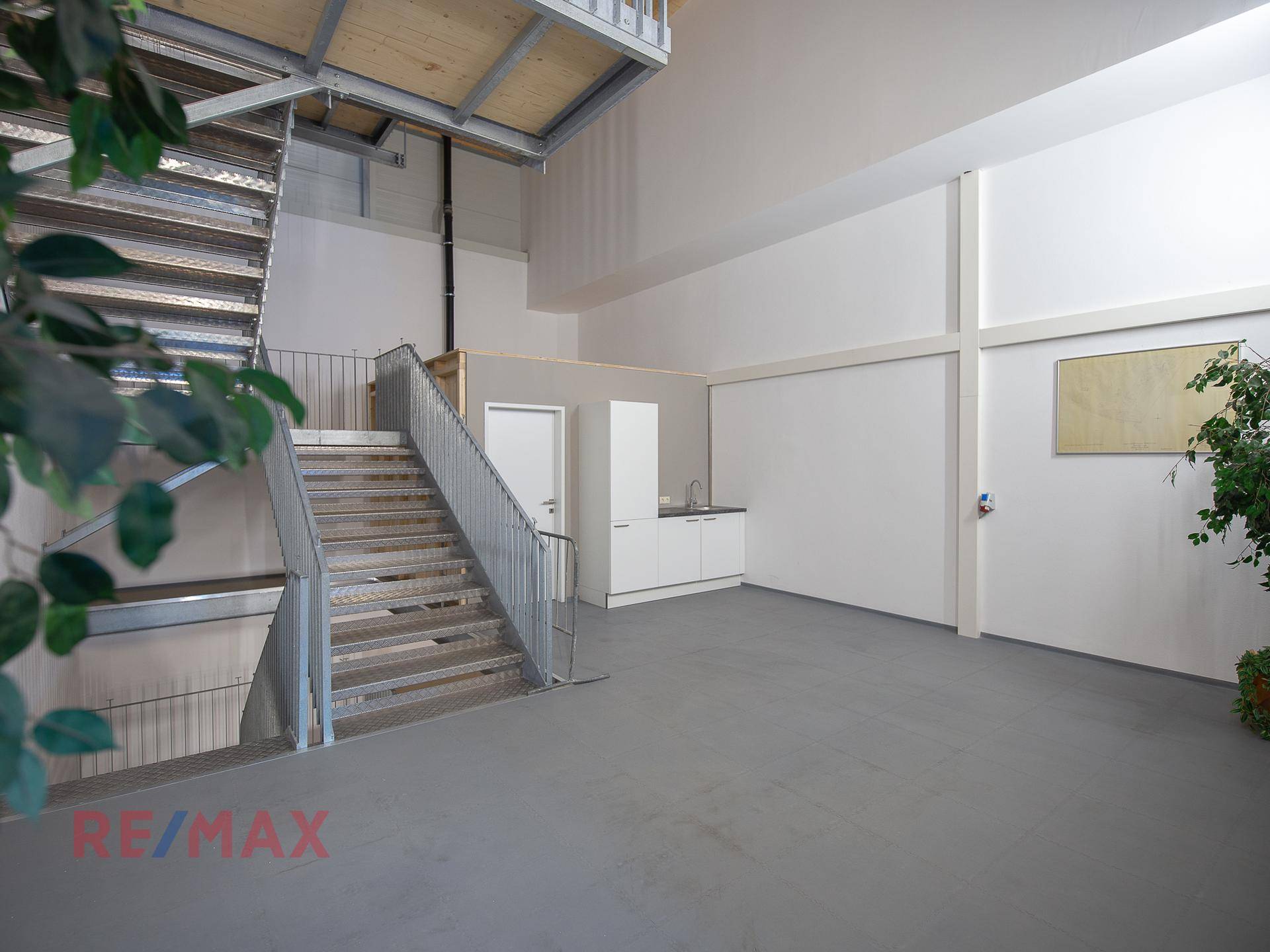 Industrielle Metalltreppe führt zu einer oberen Ebene, mit einer kleinen Küchenzeile im Hintergrund und hohen Decken.