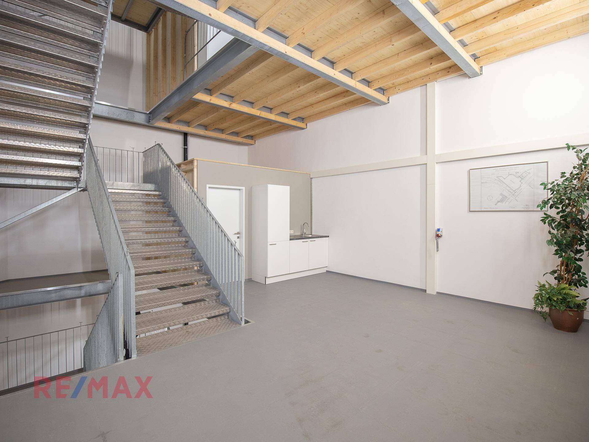 Offener Bereich mit einer Metalltreppe, einer kleinen Küchenzeile und sichtbaren Holzdeckenbalken, die Charakter verleihen.