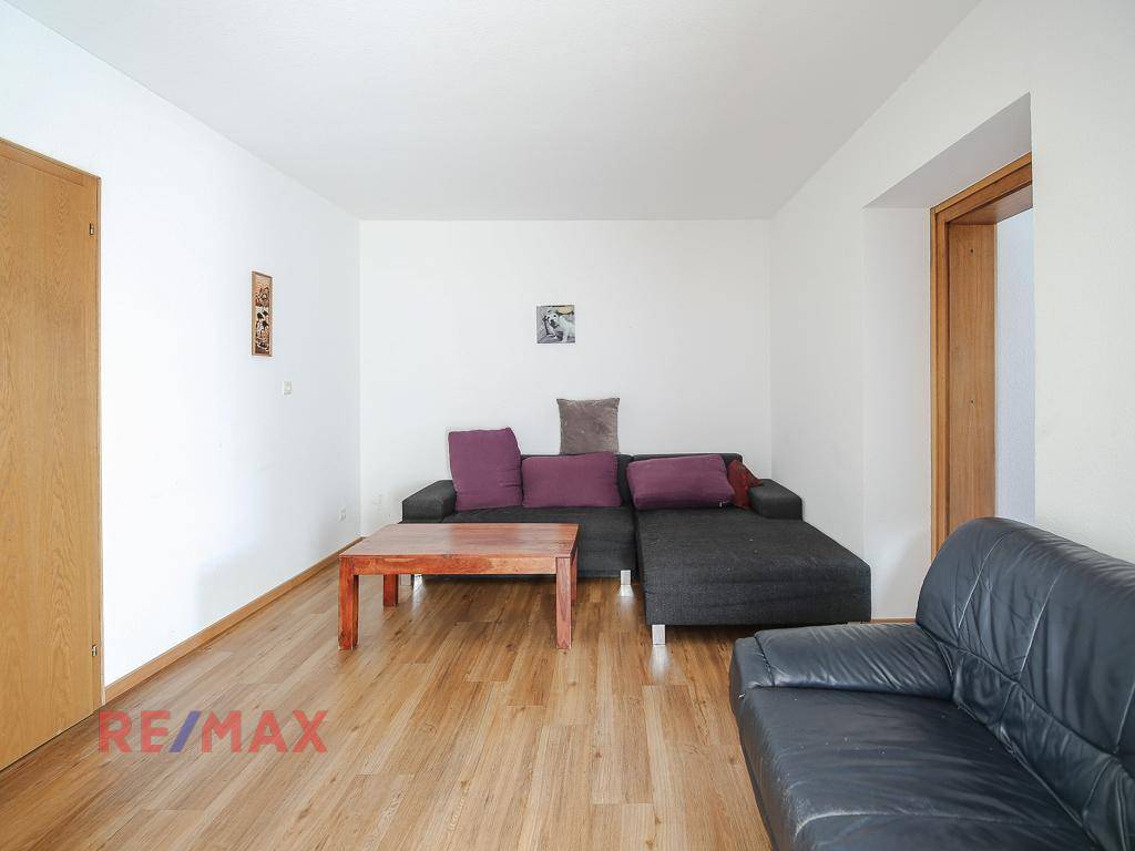 Wohnzimmer mit Holzboden, dunklem Sofa und einem Holztisch.