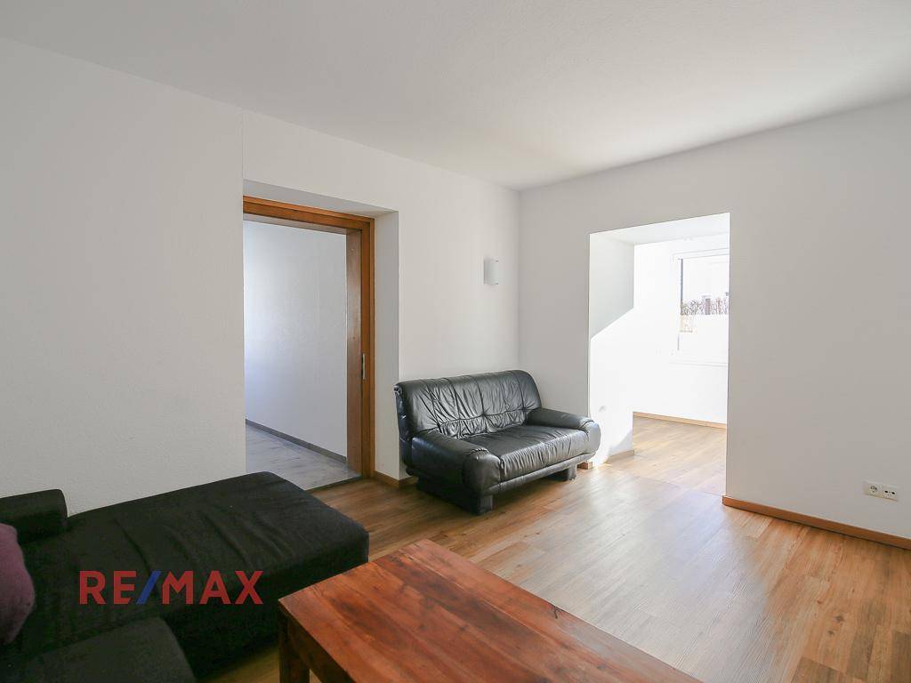 Helles Wohnzimmer mit Holzboden und Zugang zu einem weiteren Raum.
