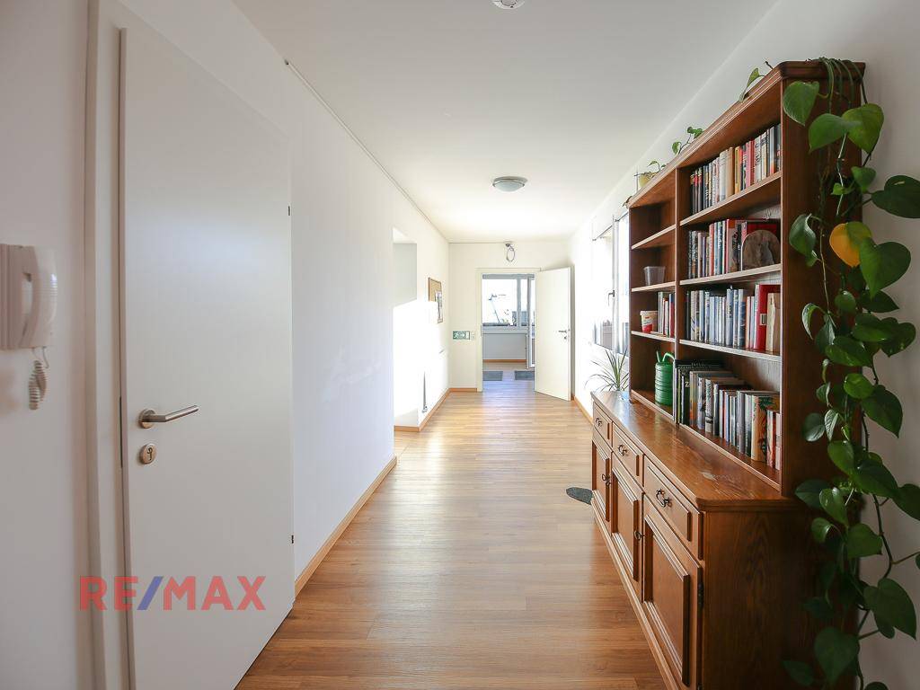 Langer Flur mit Holzboden, Bücherregal und viel natürlichem Licht.