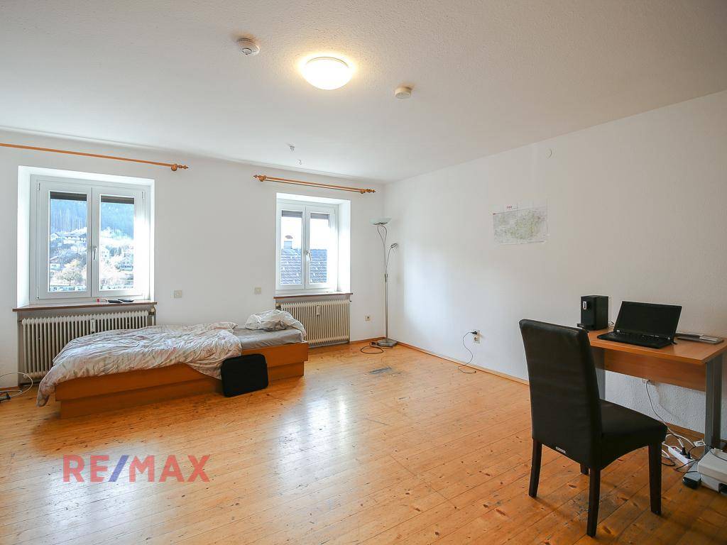 Geräumiges Schlafzimmer mit Holzboden, zwei Fenstern und einem Bett.