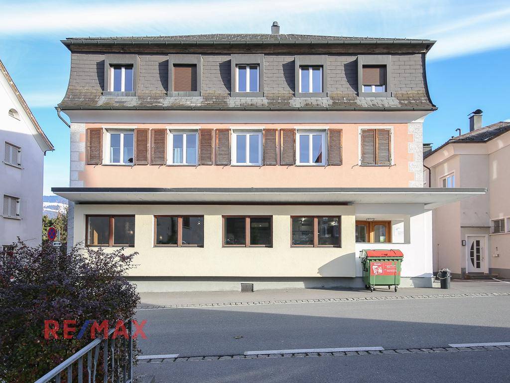 Mehrfamilienhaus mit Mansarddach und Fensterläden an einer Straße gelegen.