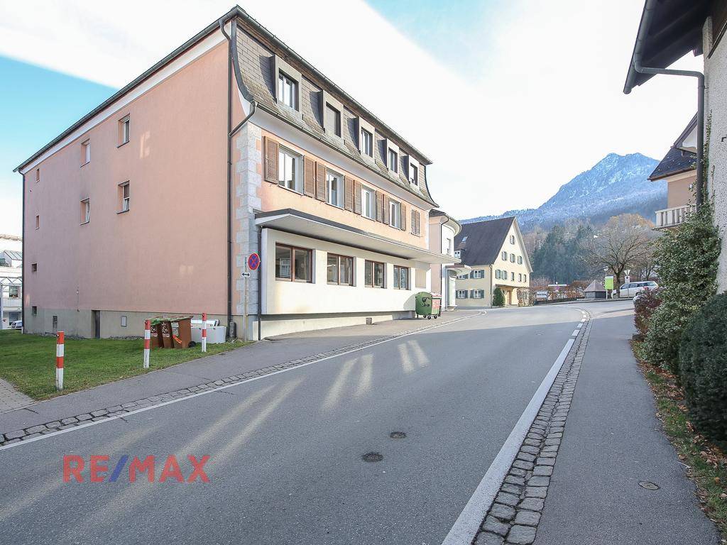 Gebäudeansicht von der Straße mit Mansarddach und umliegender Bebauung.