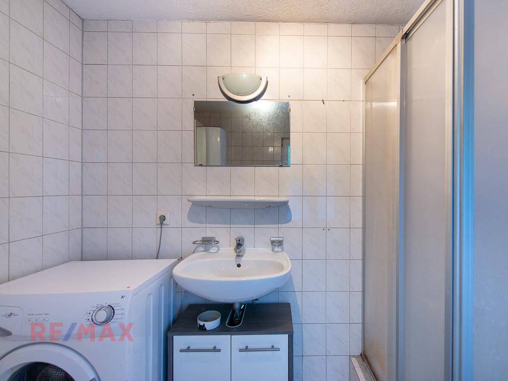 Helles Badezimmer mit Duschkabine, Waschbecken und Waschmaschine.