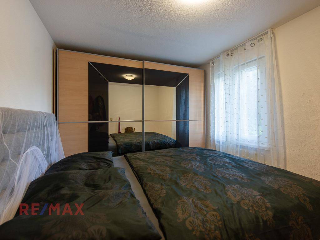 Schlafzimmer mit Doppelbett, Spiegelschiebetüren und Fenster mit Vorhängen.