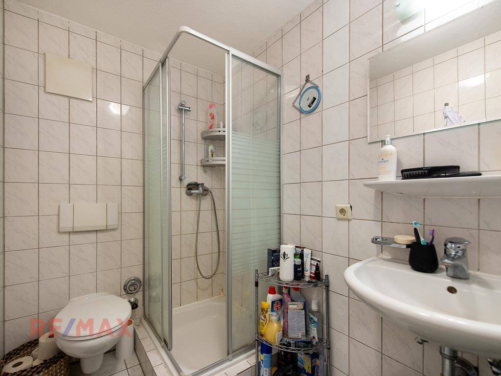 Badezimmer mit Duschkabine, WC und Waschbecken, gefliest in Weiß.