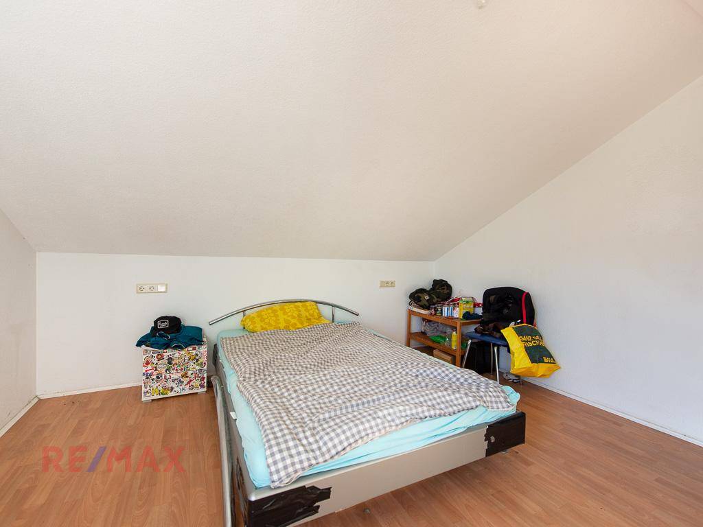 Schlafzimmer im Dachgeschoss mit schrägen Wänden, Einzelbett und Holzboden.