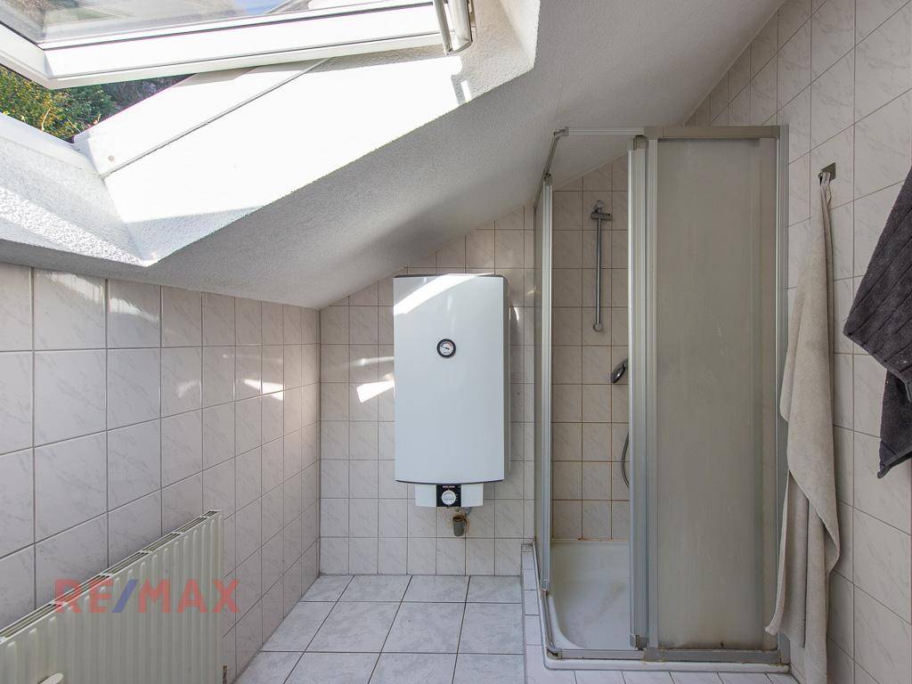 Badezimmer im Dachgeschoss mit Duschkabine, Warmwasserboiler und Fliesenboden.