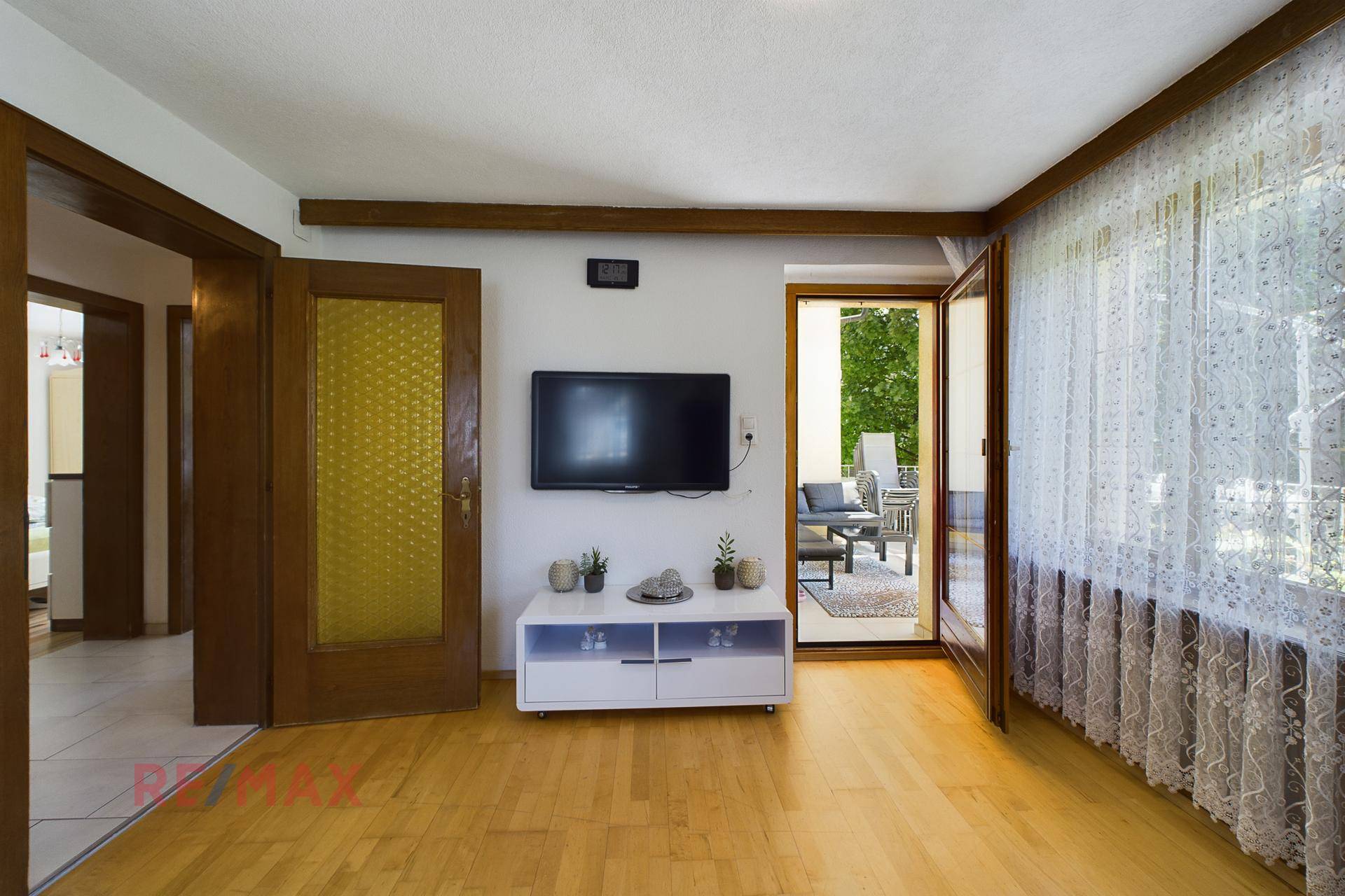 Wohnzimmer mit Fernseher, Parkettboden und direktem Zugang zur sonnigen Terrasse im Freien.