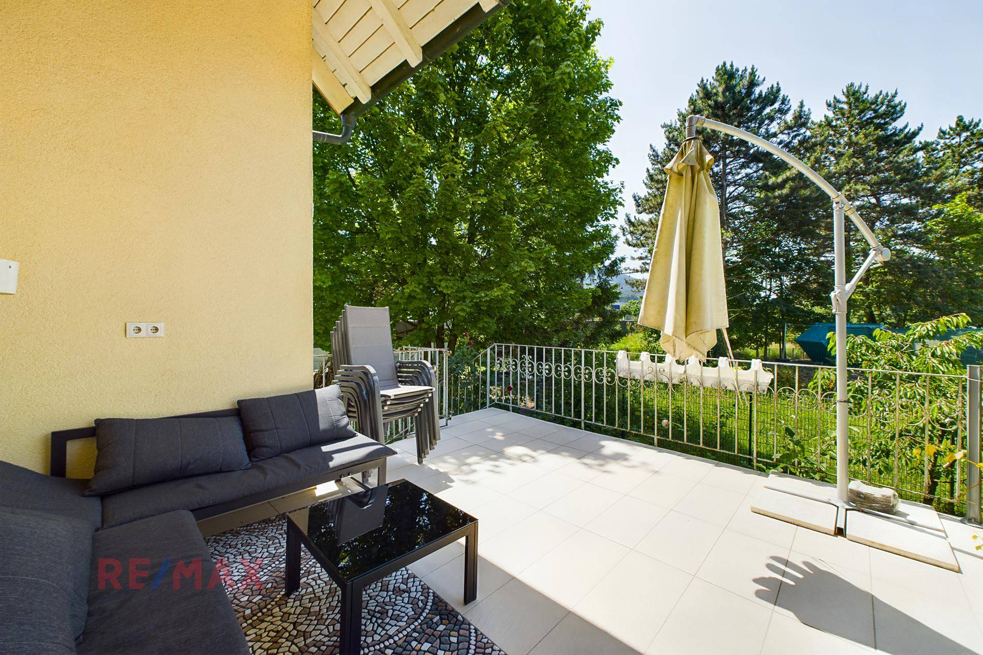 Geräumige Terrasse mit bequemen Sitzgelegenheiten, großem Sonnenschirm und Blick ins Grüne.