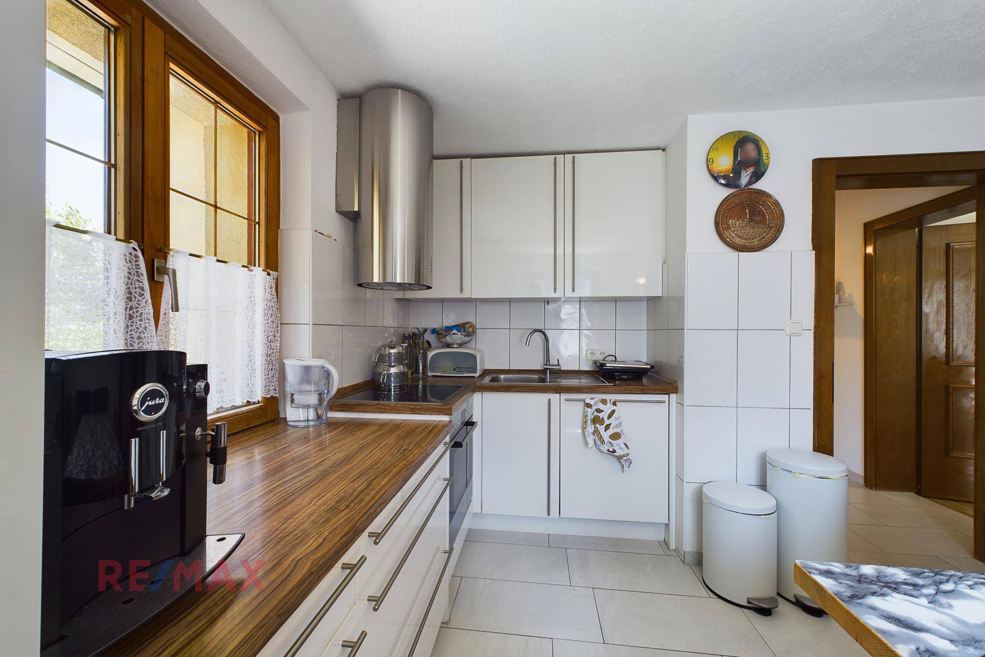 Helle Küche mit weißen Fronten, Holzdetails und einer modernen Kaffeemaschine.